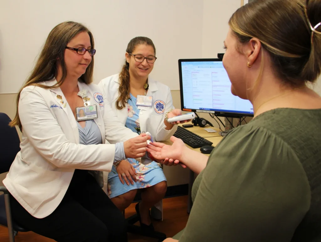 Two student doctors examine a patients hand.