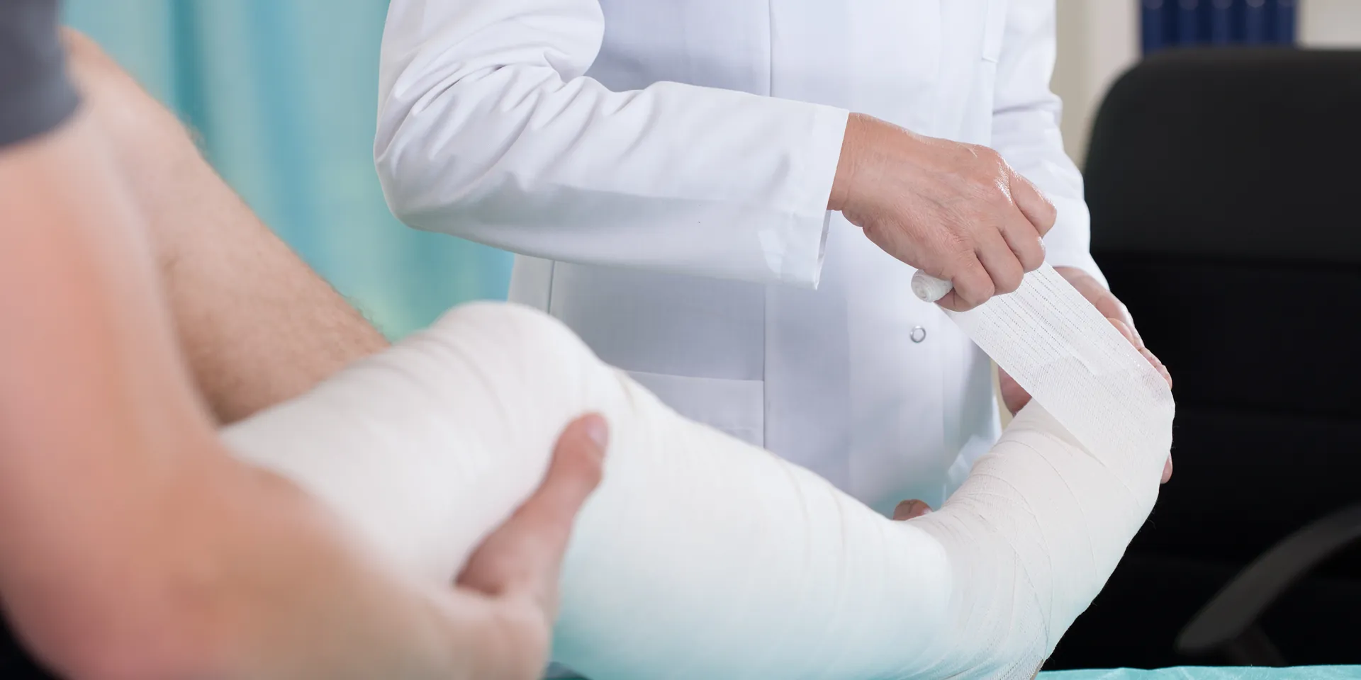 A patients lifts their leg in a cast as a doctor wraps bandages on it.